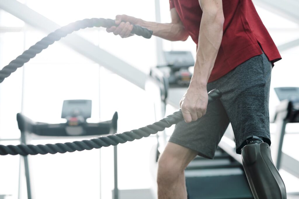 Close-up of a man with a prosthetic leg working out with battle ropes at the gym.