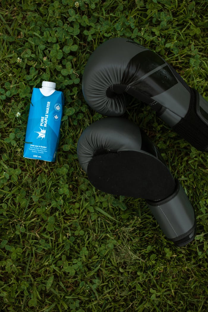 Boxing gloves and Pure Maple Water carton on grass, symbolizing hydration and fitness.